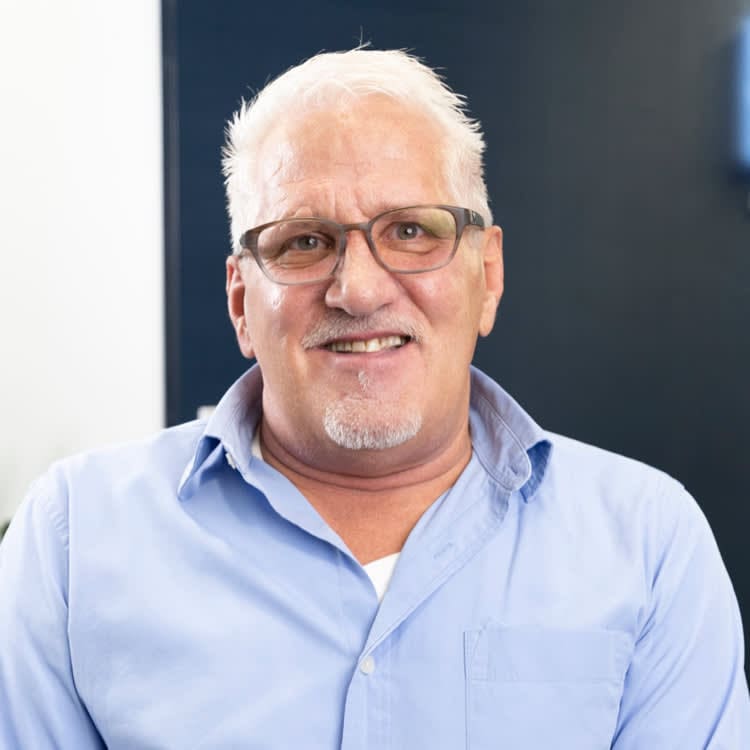 A man with glasses and white hair wearing a blue shirt.