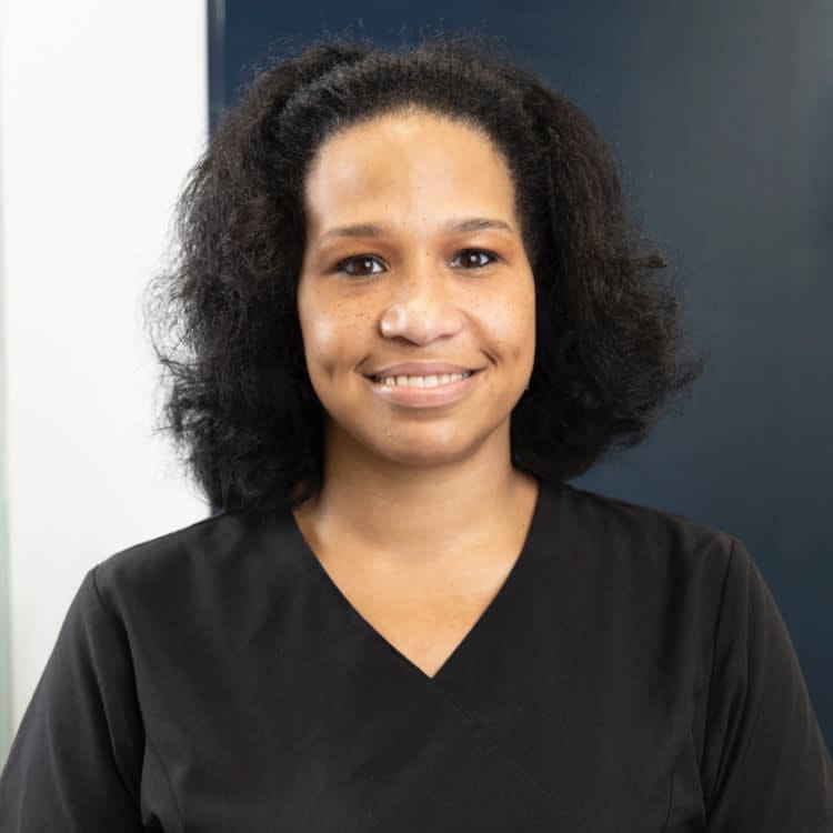 A person with shoulder-length curly hair, wearing a black top, smiles at the camera.